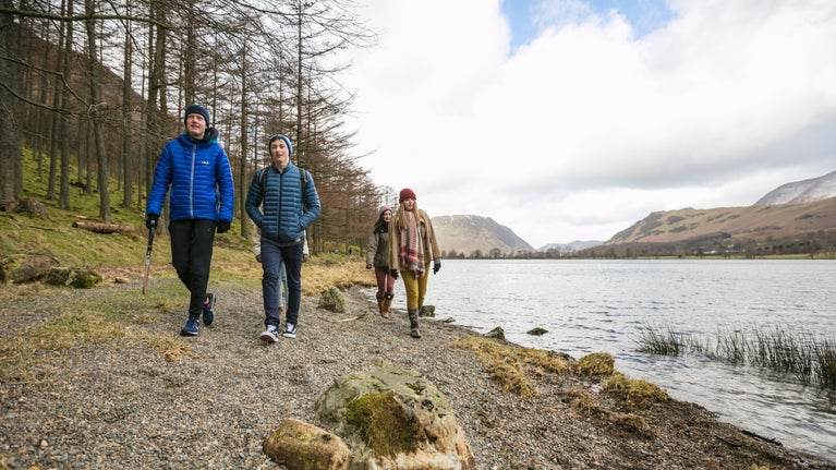 A group of people in outdoor winter clothing walk along the shore of Buttermere in Cumbria